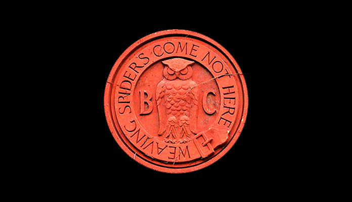 Símbolo del Bohemian Club con un búho flanqueado por las letras B y C y rodeado por el lema “Weaving Spiders Come Not Here” (Las arañas que tejen no vienen aquí)